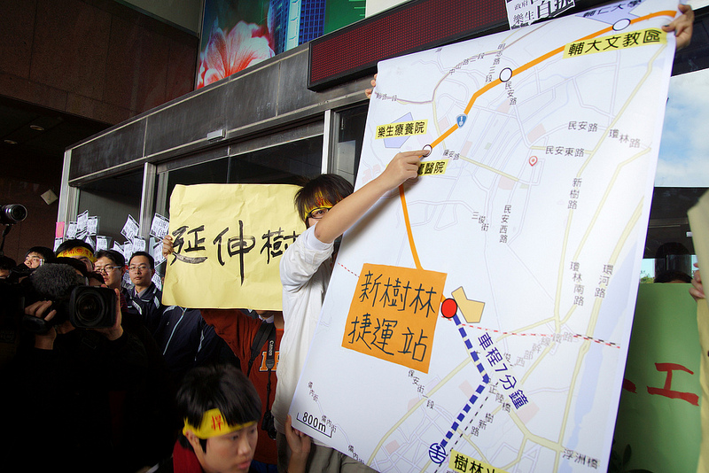 圖片說明:樂青在一次抗議行動中,說明新增設新樹林捷運站,並將機廠遷至已廢棄的台汽機料場做為儲車與維修空間,即可樂生和捷運雙贏。圖片來源:苦勞網,攝影:陳韋綸。